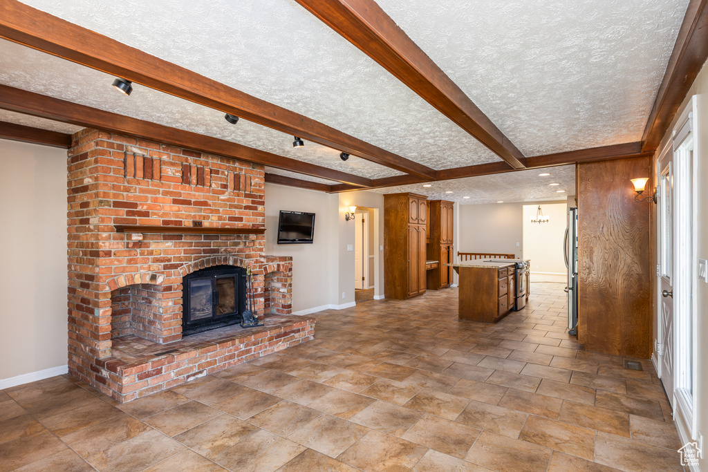 Unfurnished living room featuring a brick fireplace, stone finish flooring, a textured ceiling, and beam ceiling