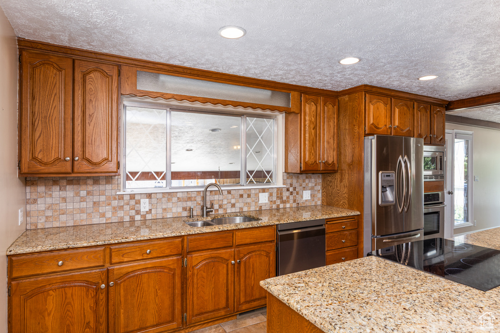 Kitchen with stainless steel appliances, a textured ceiling, brown cabinets, decorative backsplash, and recessed lighting
