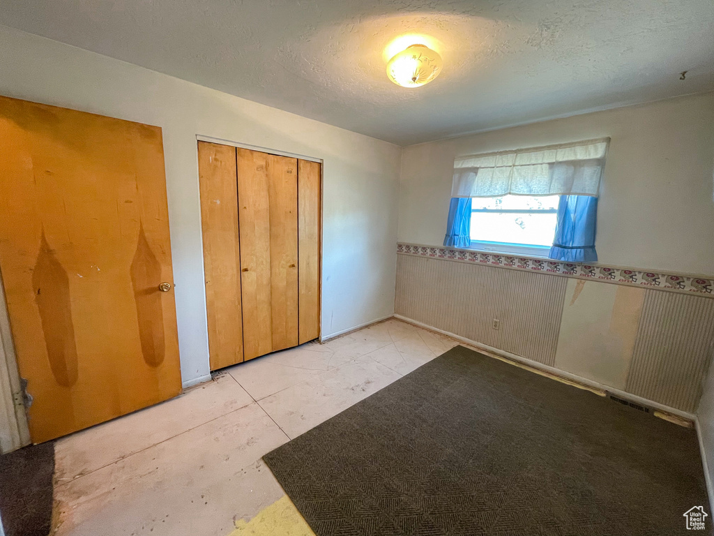 Unfurnished bedroom with wainscoting, a closet, and a textured ceiling