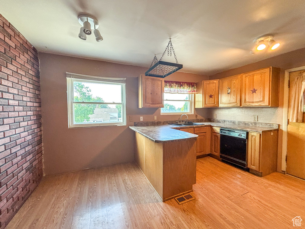 Kitchen featuring dishwasher, a peninsula, light wood-type flooring, brick wall, and dark countertops