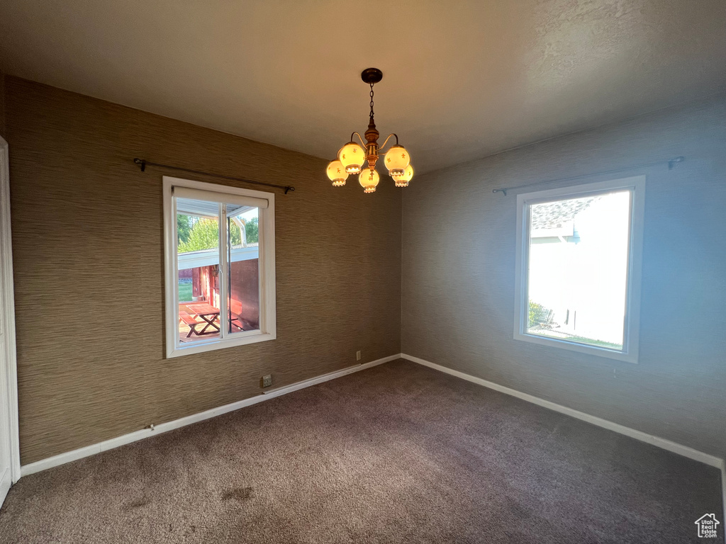 Carpeted empty room with a chandelier and baseboards
