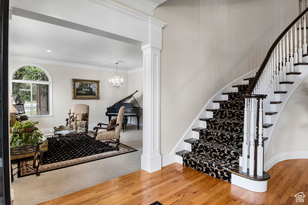 Stairs with ornate columns, wood finished floors, crown molding, and a chandelier