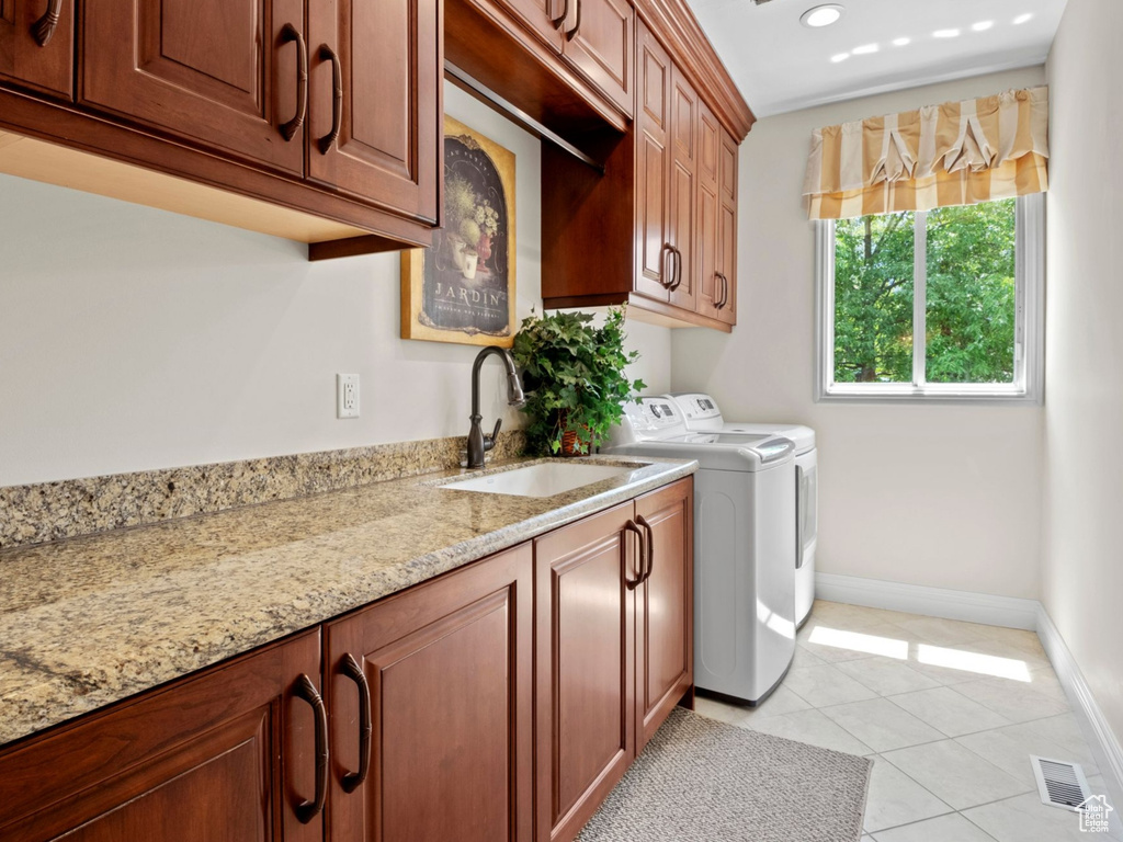 Washroom featuring washing machine and clothes dryer, cabinet space, and light tile patterned flooring