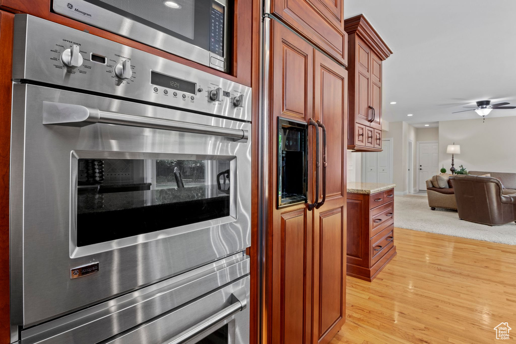 Kitchen featuring appliances with stainless steel finishes, light stone countertops, open floor plan, light wood-style flooring, and a ceiling fan
