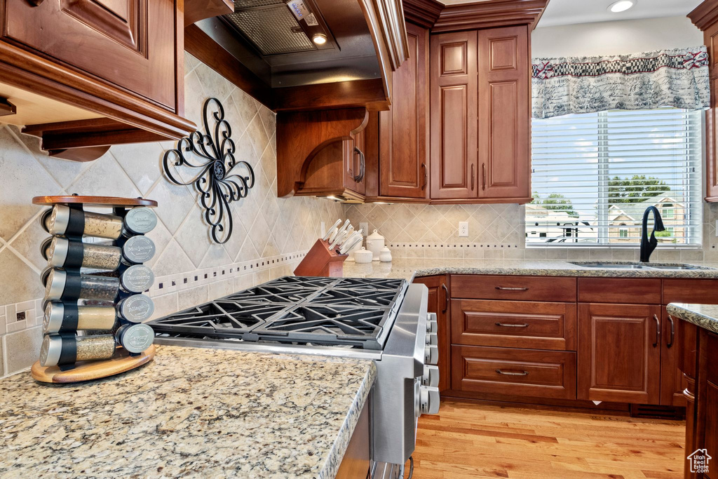 Kitchen featuring stainless steel range oven, custom range hood, tasteful backsplash, light wood-style flooring, and light stone countertops