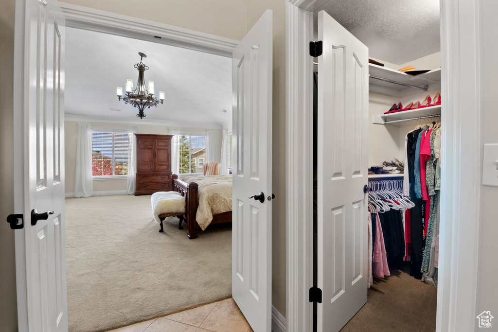 Corridor with light colored carpet, a chandelier, and light tile patterned floors