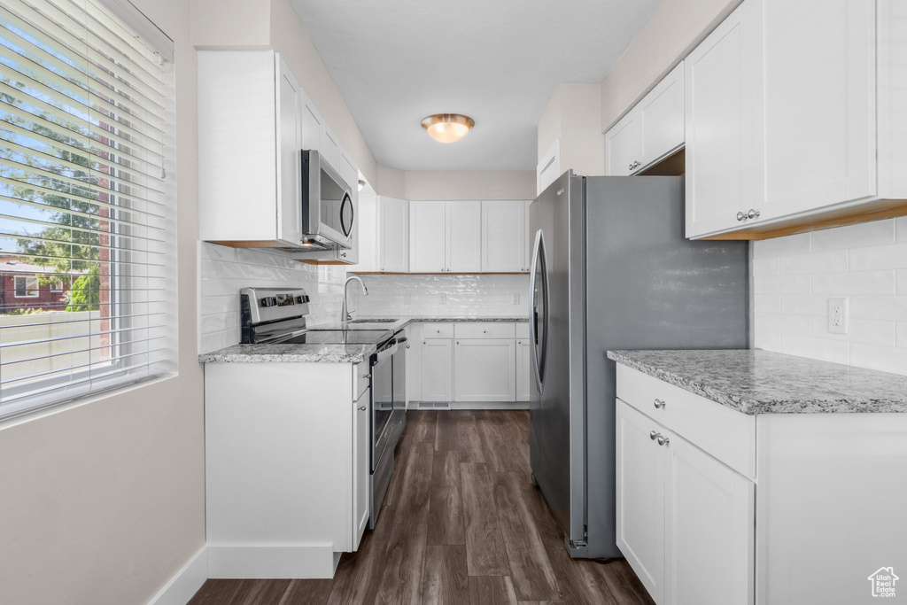 Kitchen with appliances with stainless steel finishes, dark wood-style floors, backsplash, white cabinets, and light stone countertops