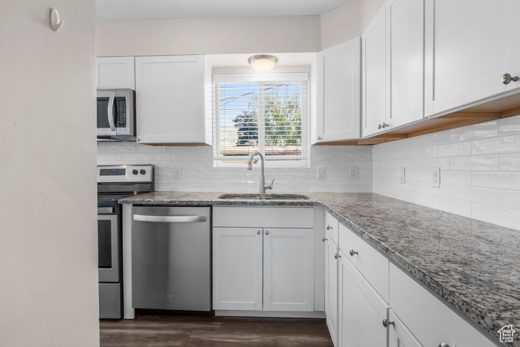 Kitchen with stainless steel appliances, dark wood-style floors, white cabinetry, light stone countertops, and tasteful backsplash