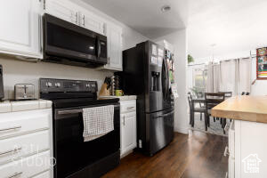 Kitchen with black appliances, white cabinets, dark wood-style floors, and wooden counters