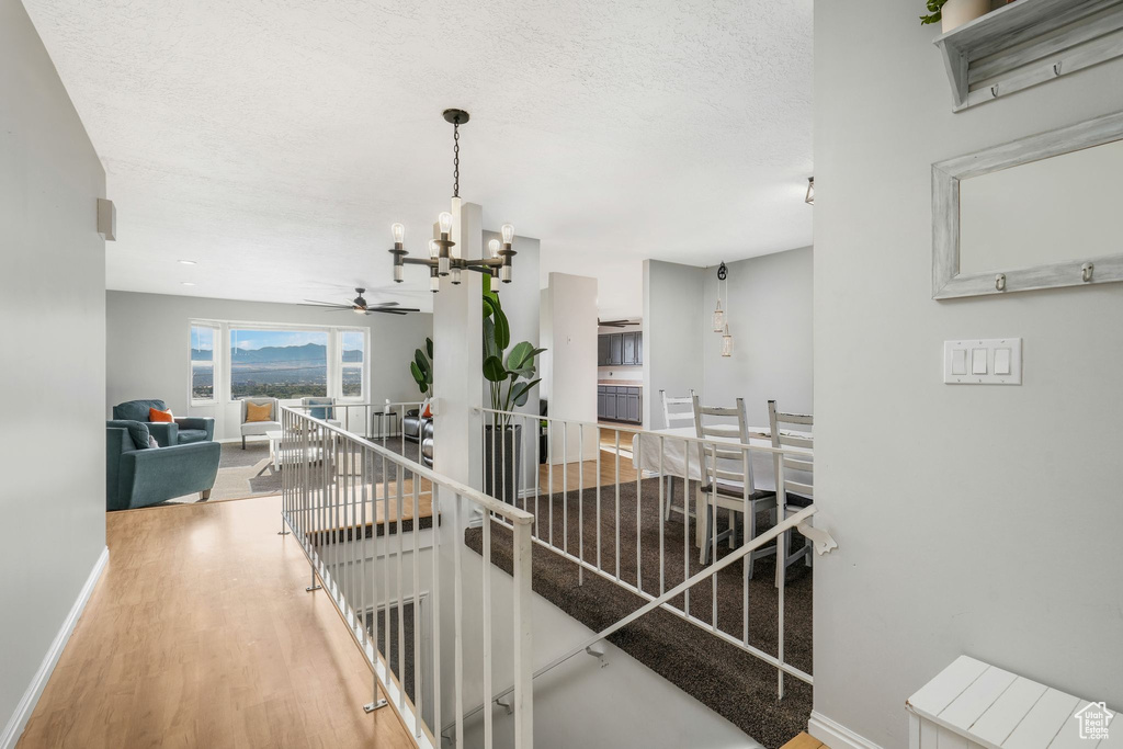 Hallway with an upstairs landing, a chandelier, wood finished floors, and a textured ceiling