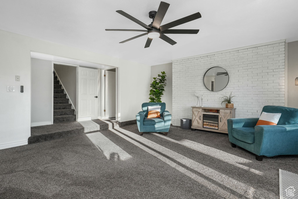 Carpeted living room featuring stairway, ceiling fan, and brick wall