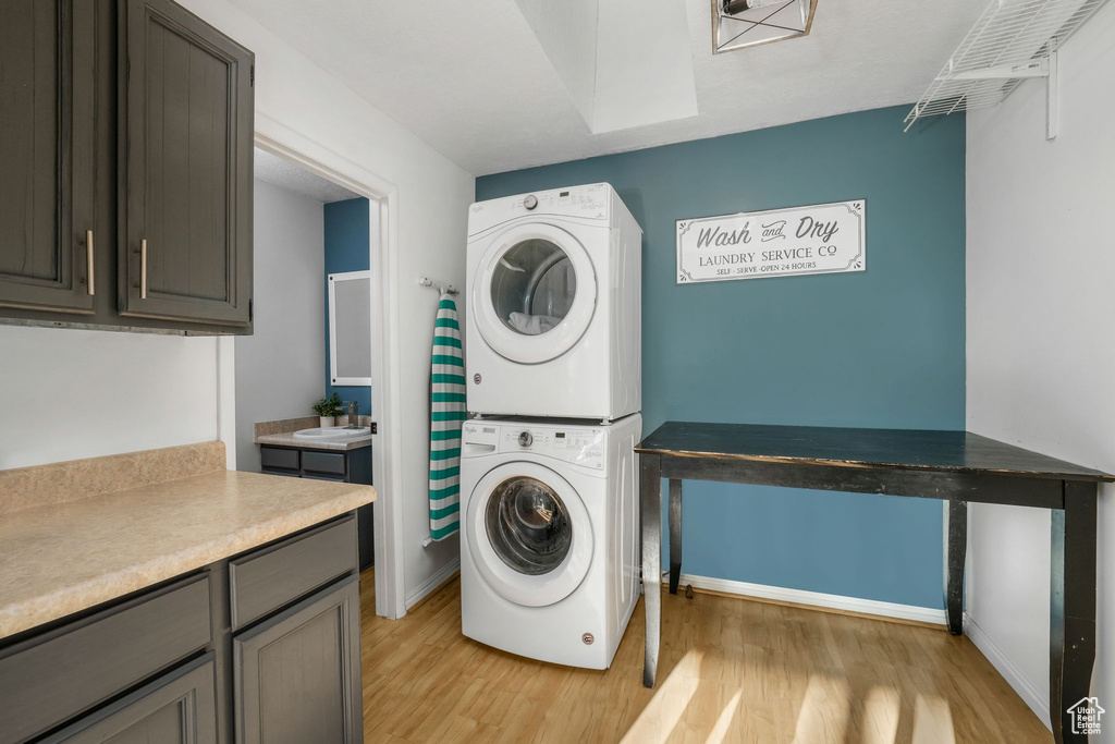 Laundry room featuring stacked washer and clothes dryer, cabinet space, and light wood finished floors