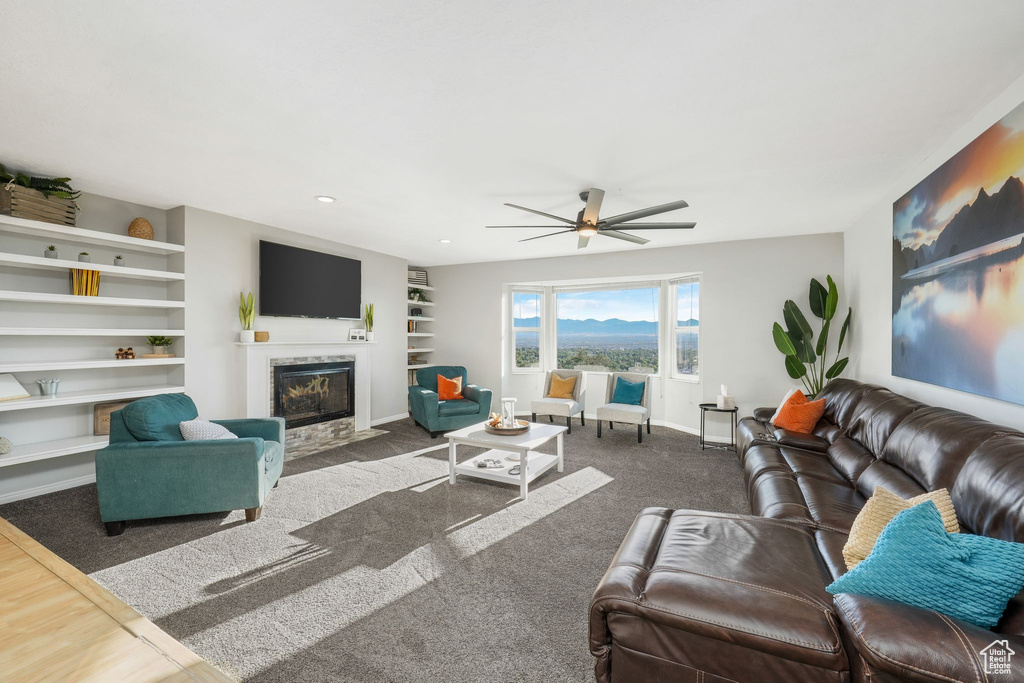 Carpeted living room with a fireplace with flush hearth and ceiling fan