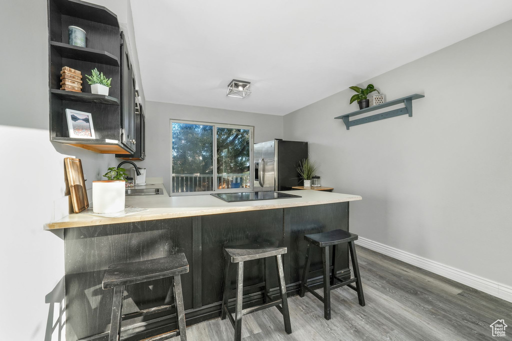 Kitchen with stainless steel refrigerator with ice dispenser, open shelves, wood finished floors, black electric stovetop, and light countertops