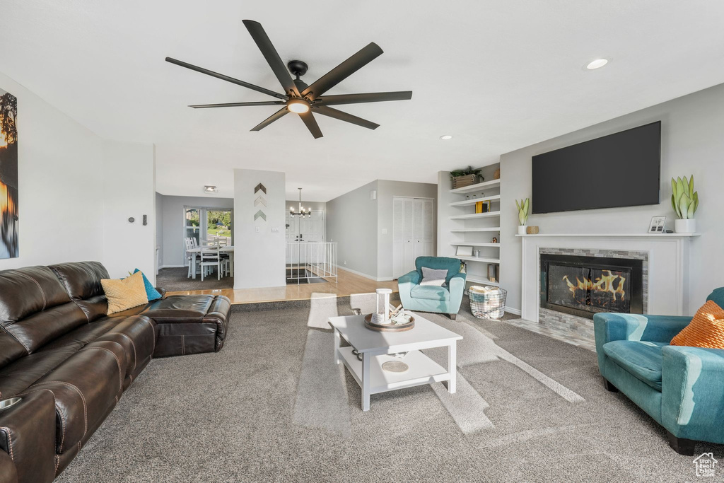 Living room featuring a fireplace with flush hearth, a ceiling fan, a chandelier, recessed lighting, and built in shelves