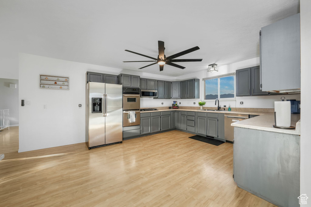 Kitchen featuring appliances with stainless steel finishes, gray cabinetry, ceiling fan, light wood-style floors, and light countertops