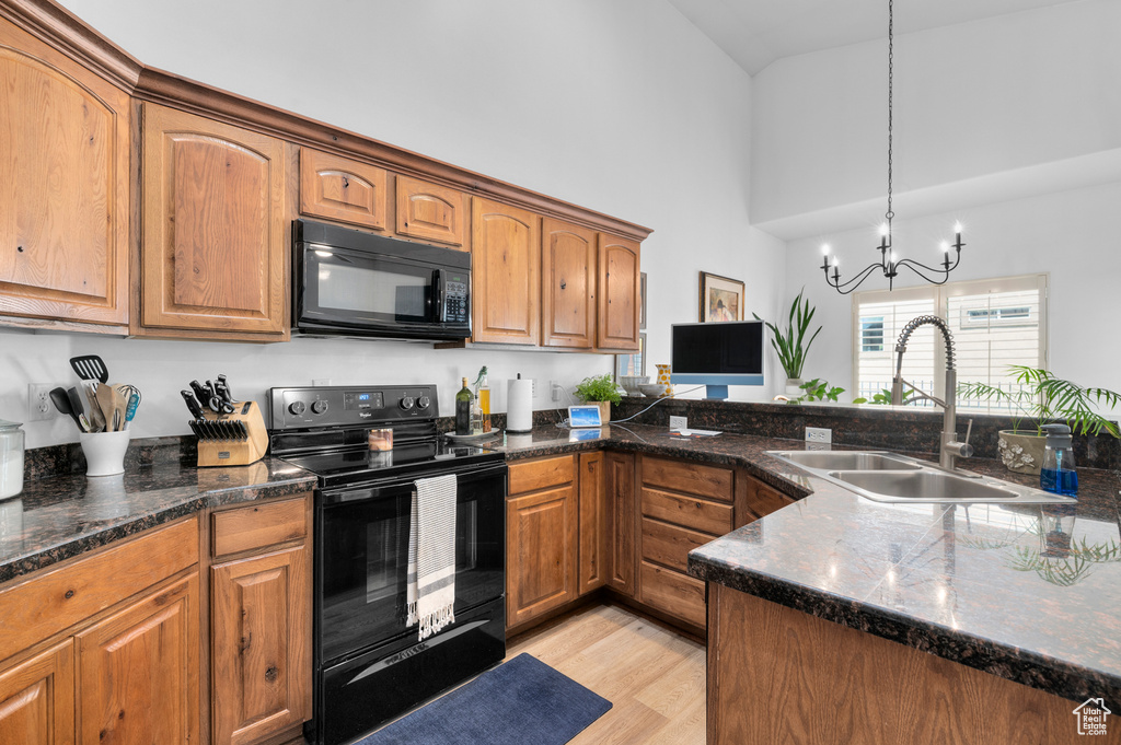 Kitchen with black appliances, a high ceiling, light wood-type flooring, brown cabinetry, and dark stone countertops