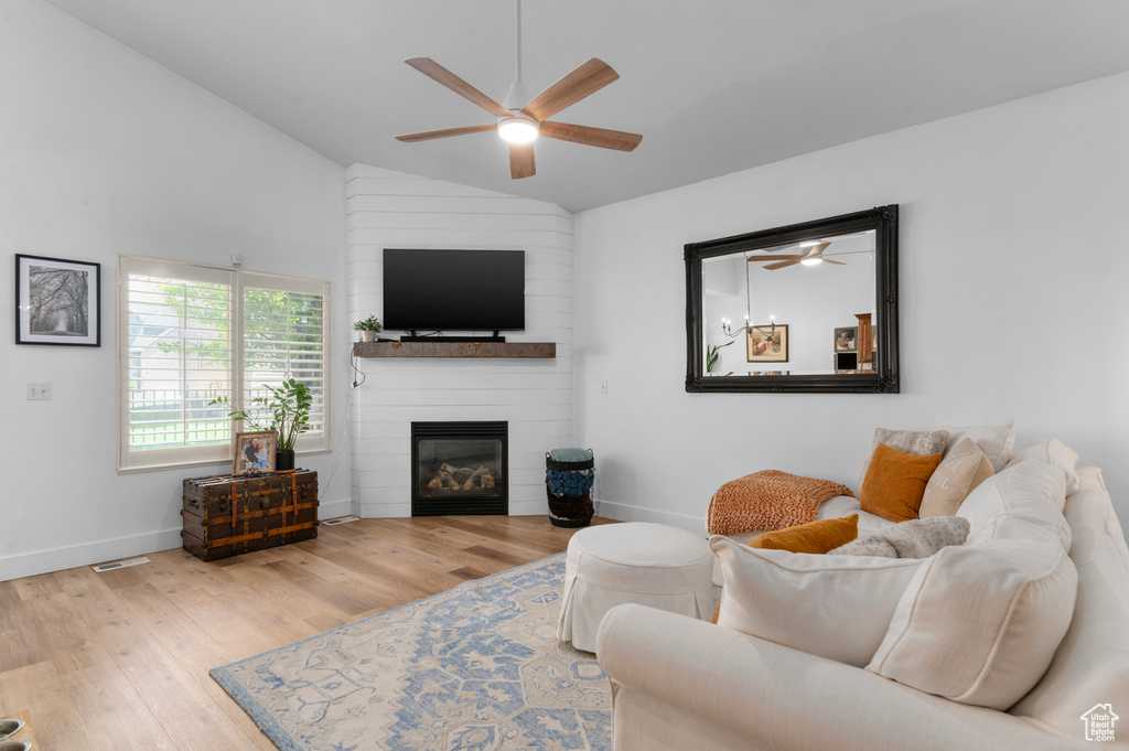 Living room with ceiling fan, wood finished floors, a large fireplace, and high vaulted ceiling
