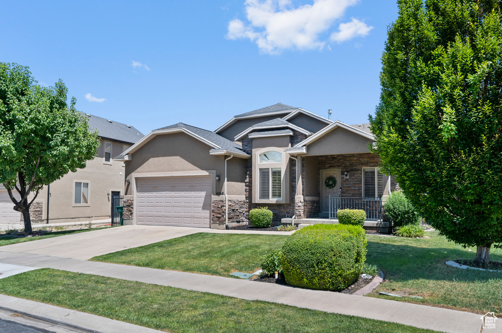 View of front of home with an attached garage, stone siding, stucco siding, concrete driveway, and a front yard