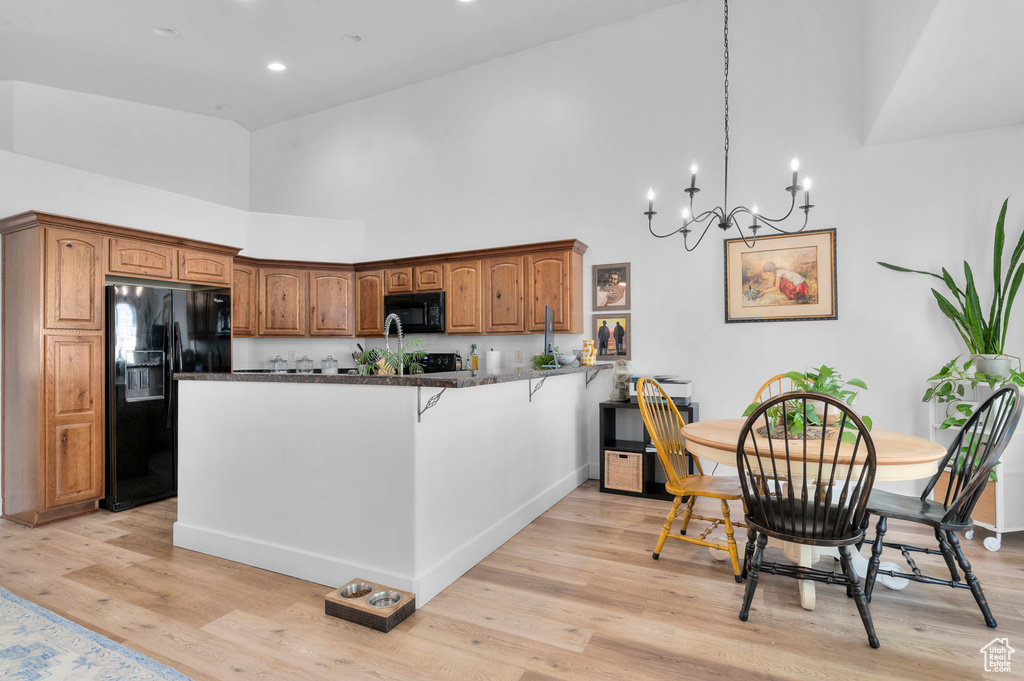 Kitchen featuring high vaulted ceiling, a peninsula, black appliances, light wood-style floors, and a chandelier