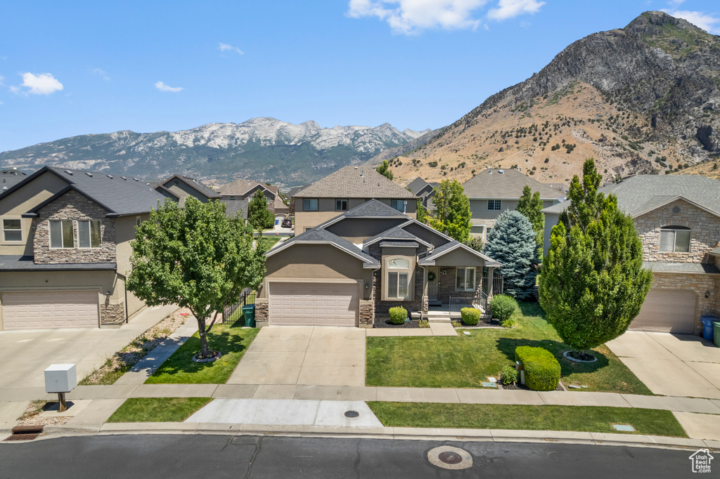 View of front facade with driveway, a garage, stone siding, a mountain view, and a front lawn