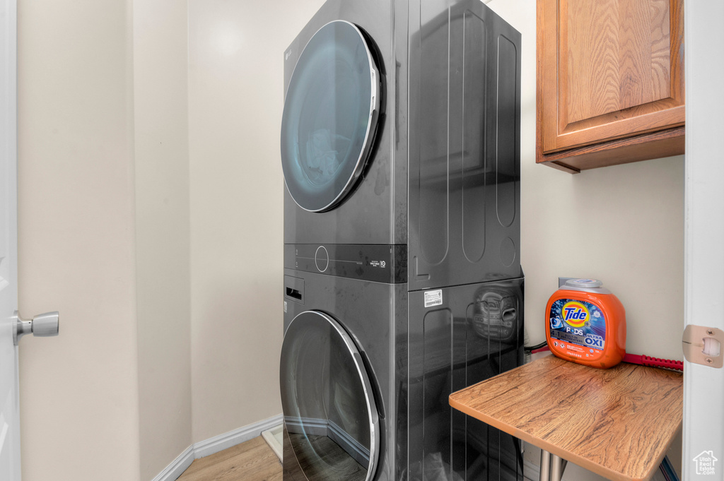 Washroom with stacked washer / drying machine, cabinet space, and wood finished floors