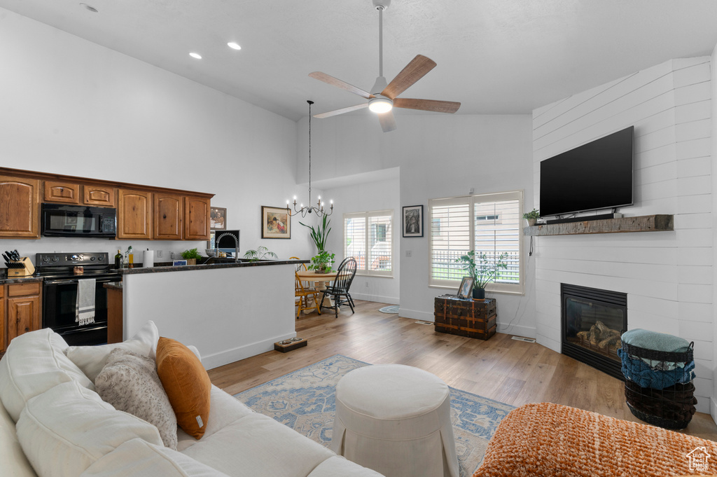 Living area with high vaulted ceiling, ceiling fan, a large fireplace, light wood finished floors, and a chandelier