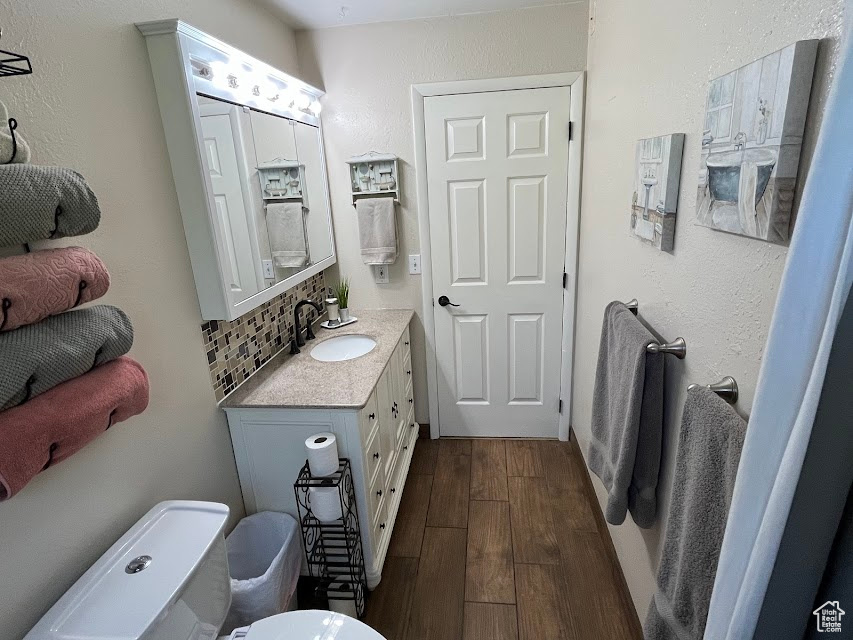 Half bath with vanity, wood finished floors, and decorative backsplash