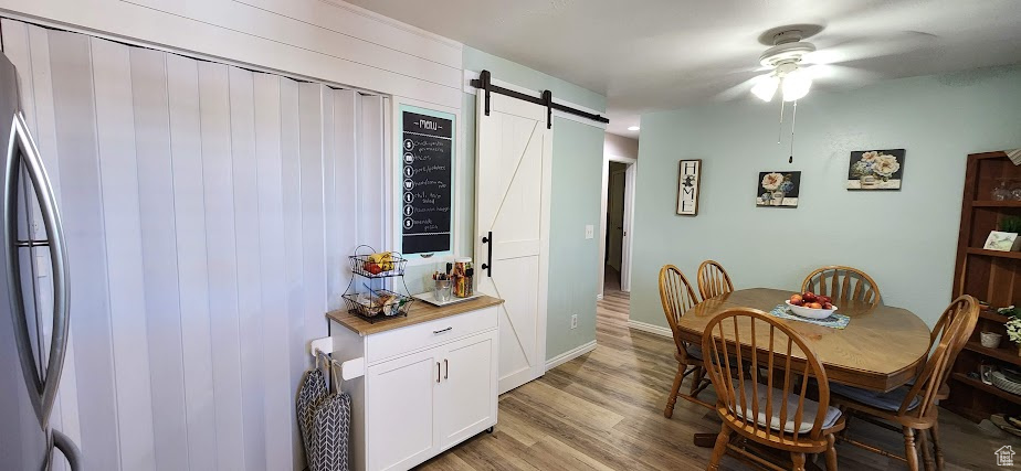 Dining space featuring ceiling fan, a barn door, and light wood finished floors
