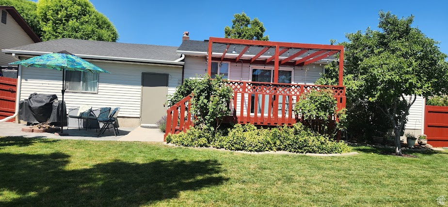 Rear view of house with a pergola, a yard, a chimney, a wooden deck, and a patio