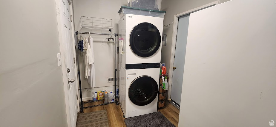 Laundry room with stacked washer and clothes dryer and wood finished floors