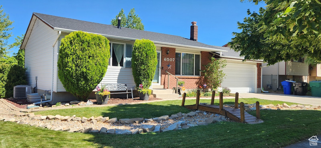 Ranch-style home featuring a chimney, concrete driveway, an attached garage, a front yard, and brick siding