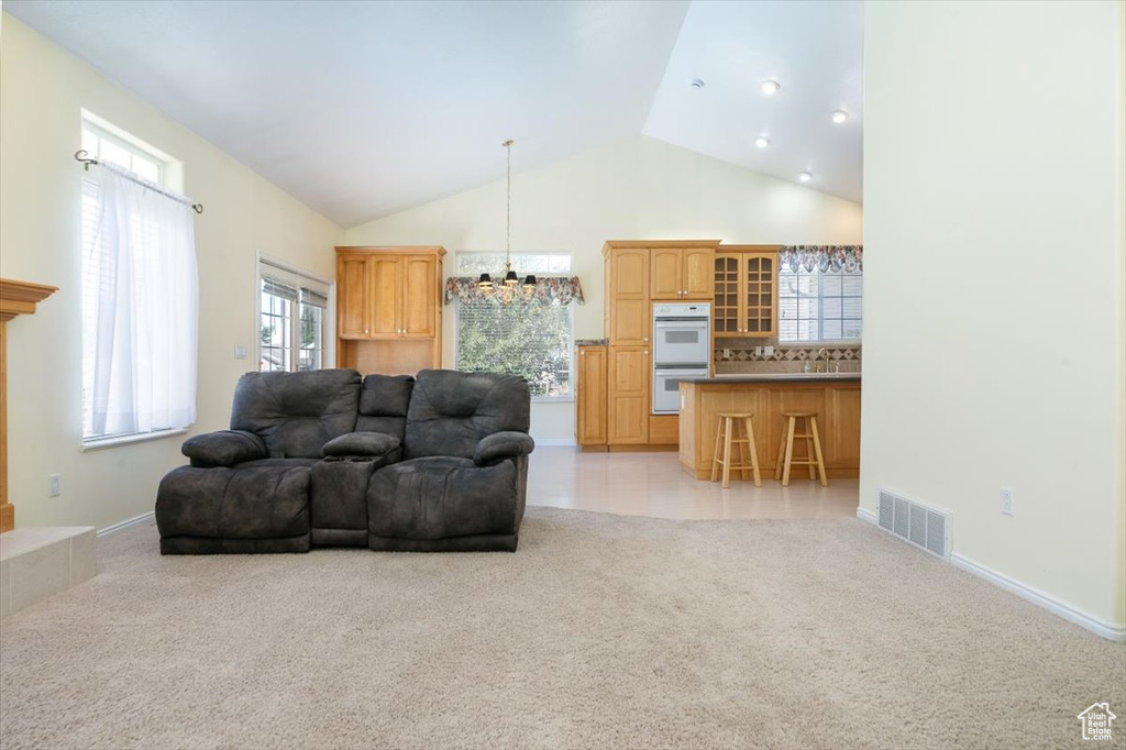 Living area with a chandelier, light carpet, and high vaulted ceiling