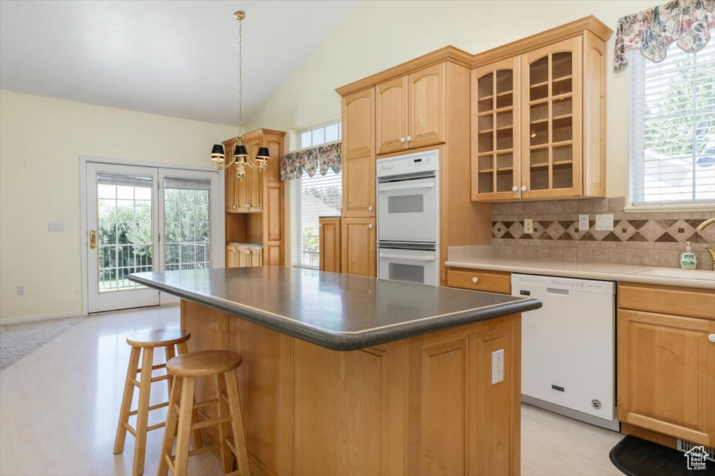 Kitchen with vaulted ceiling, white appliances, a chandelier, a breakfast bar area, and a center island