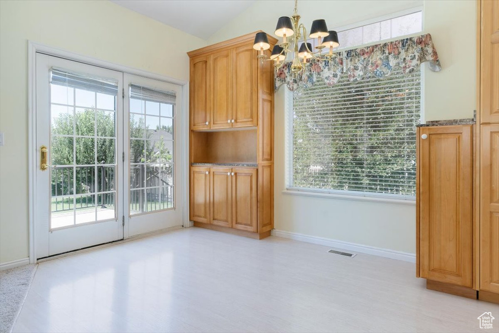 Unfurnished dining area featuring a chandelier, plenty of natural light, light wood finished floors, and lofted ceiling