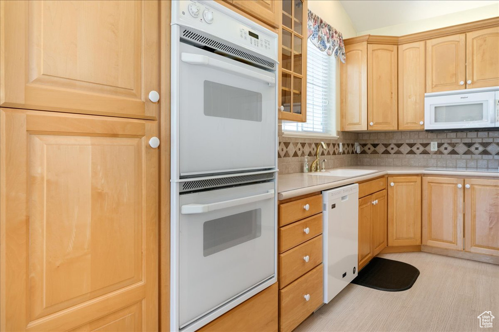 Kitchen with white appliances, light brown cabinets, light countertops, backsplash, and glass insert cabinets