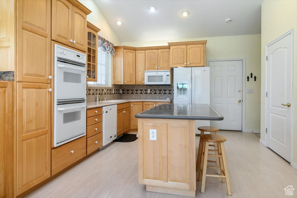 Kitchen featuring white appliances, a kitchen breakfast bar, a kitchen island, tasteful backsplash, and glass insert cabinets