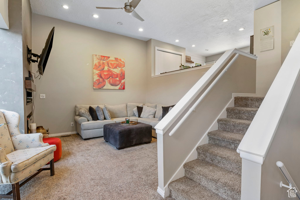 Carpeted living area with recessed lighting, ceiling fan, and stairs