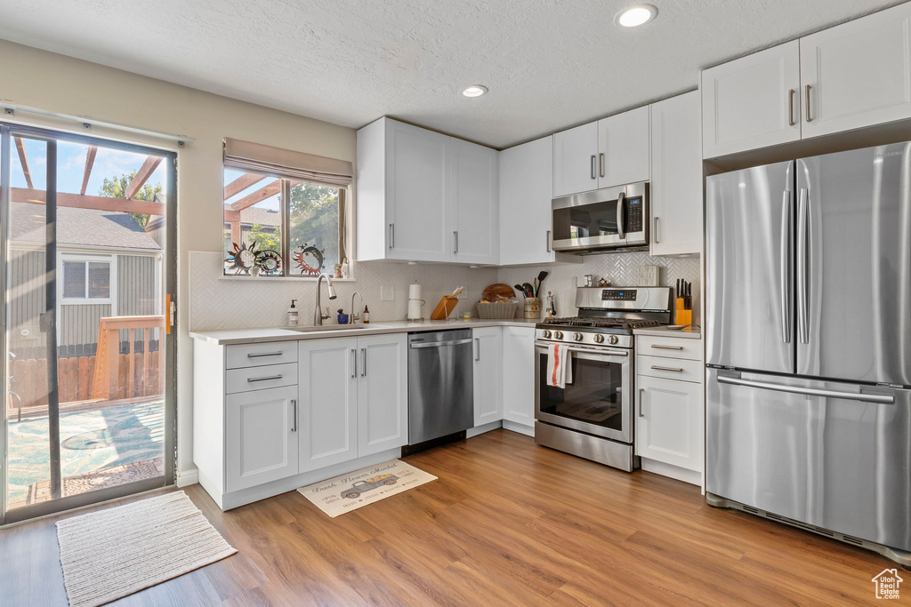 Kitchen with stainless steel appliances, light countertops, light wood finished floors, recessed lighting, and white cabinets