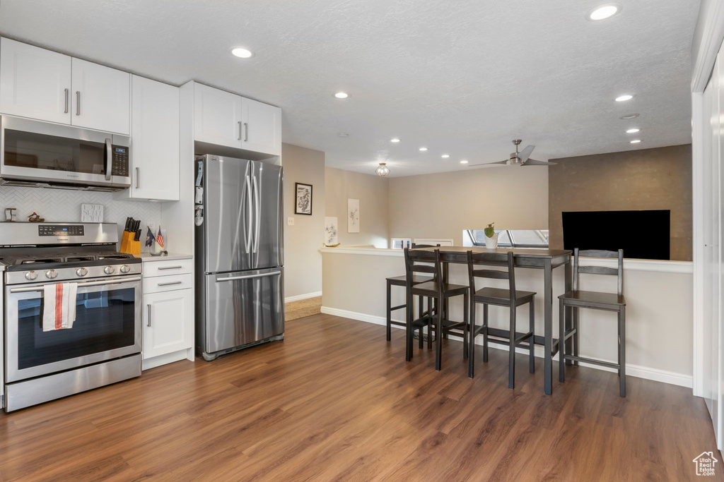 Kitchen with appliances with stainless steel finishes, recessed lighting, white cabinets, wood finished floors, and tasteful backsplash