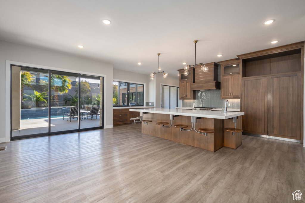 Kitchen featuring light countertops, light wood finished floors, recessed lighting, a large island with sink, and tasteful backsplash