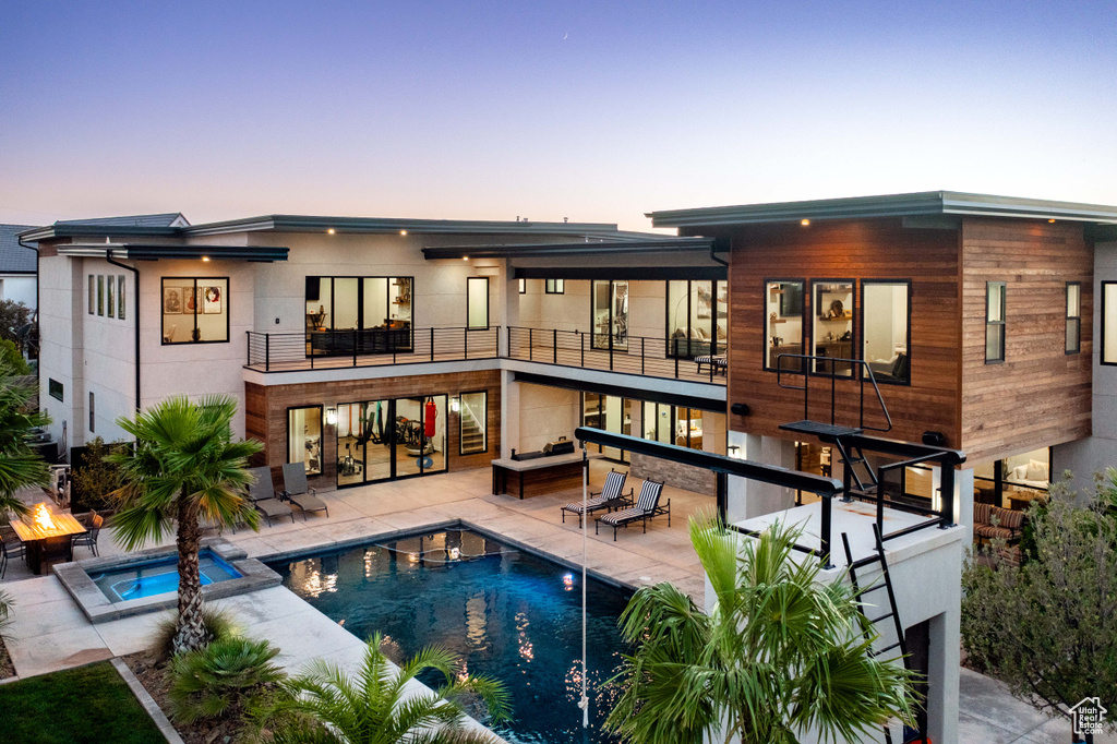 Back of property featuring a balcony, a pool with connected hot tub, a patio, an outdoor living space, and stairs
