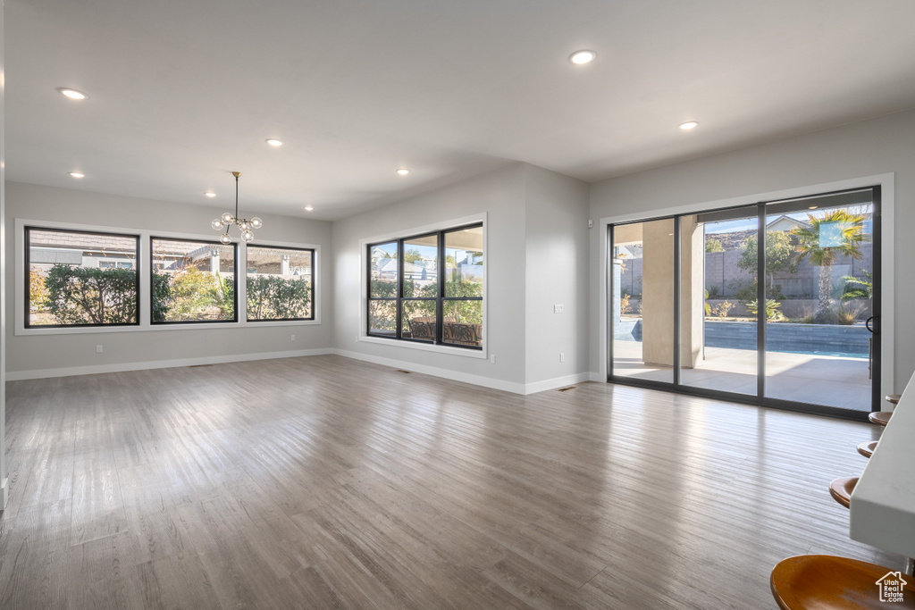 Unfurnished living room featuring healthy amount of natural light, wood finished floors, recessed lighting, and a chandelier