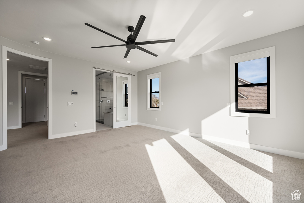 Unfurnished bedroom with light colored carpet, recessed lighting, a barn door, connected bathroom, and a ceiling fan