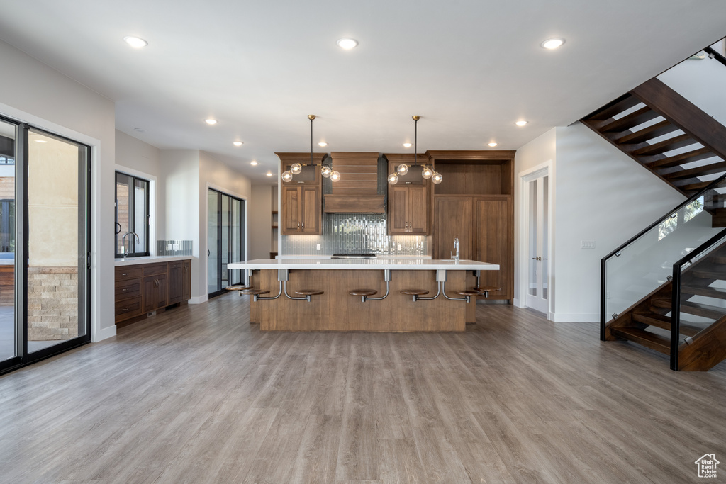 Kitchen with light countertops, tasteful backsplash, a kitchen breakfast bar, custom range hood, and light wood-type flooring