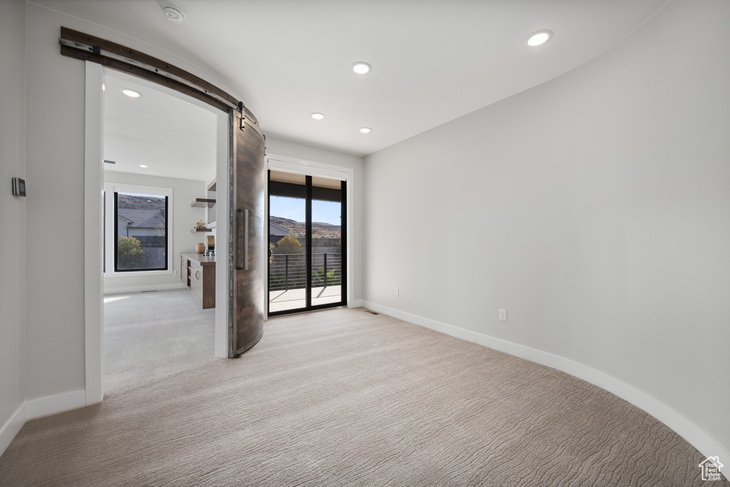 Empty room with a barn door, light colored carpet, and recessed lighting