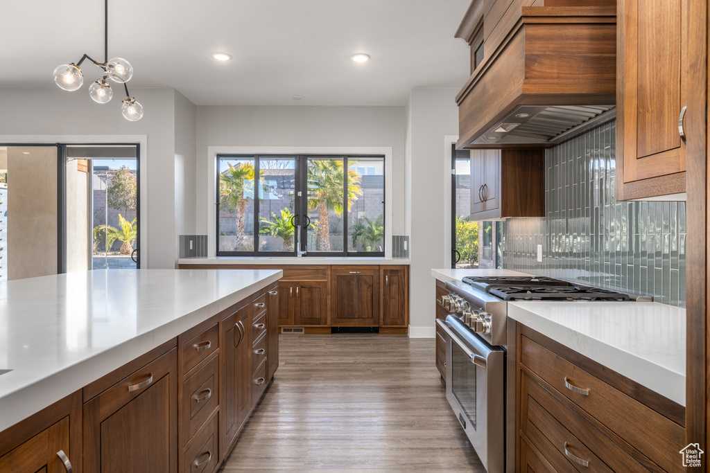Kitchen with high end stove, backsplash, light wood-type flooring, premium range hood, and light countertops