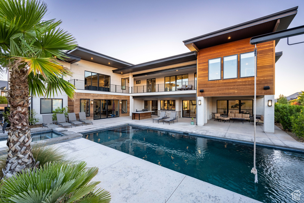 Rear view of house with a balcony, an outdoor living space, a patio, a pool with connected hot tub, and outdoor dining area
