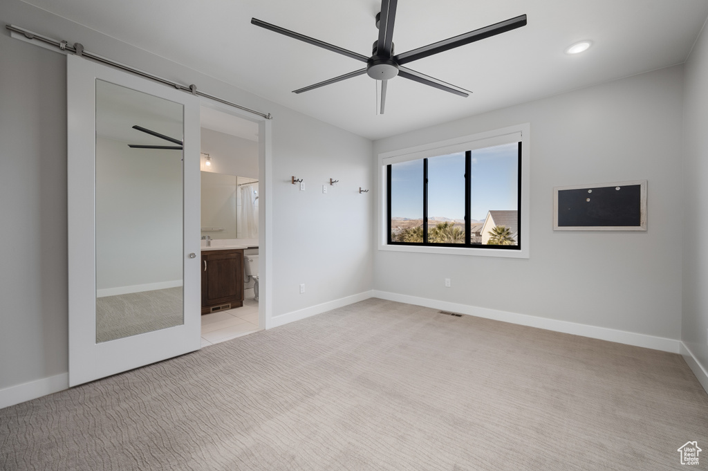 Unfurnished bedroom featuring light carpet, a barn door, recessed lighting, ensuite bath, and ceiling fan