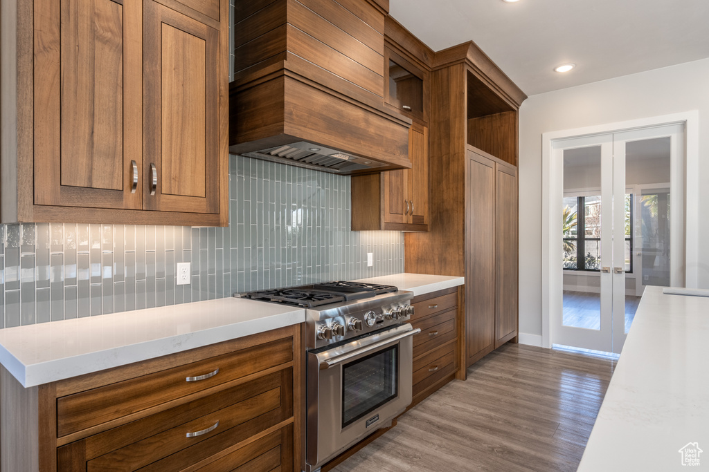 Kitchen with high end stainless steel range, french doors, custom exhaust hood, decorative backsplash, and recessed lighting